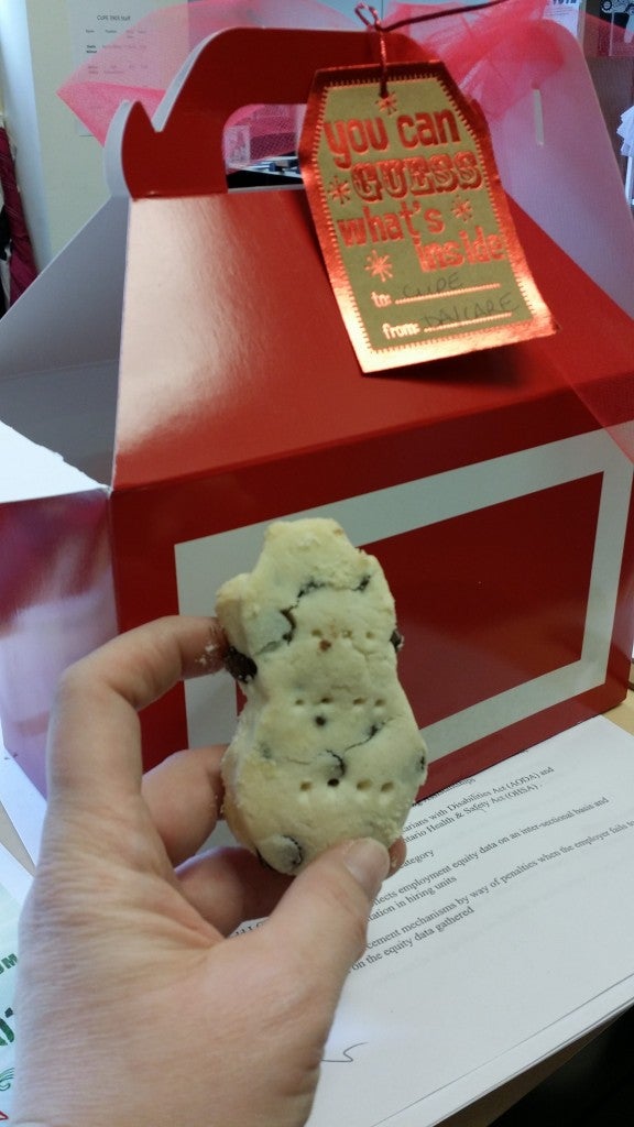 Photo: A hand holding a shortbread cookie, and a red box with a card reading "you can guess what's inside! To: CUPE. From: Daycare."