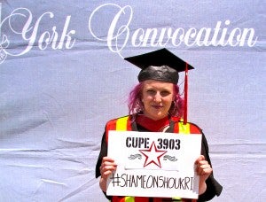 A graduating member holds a #shameonshoukri sign at convocation.